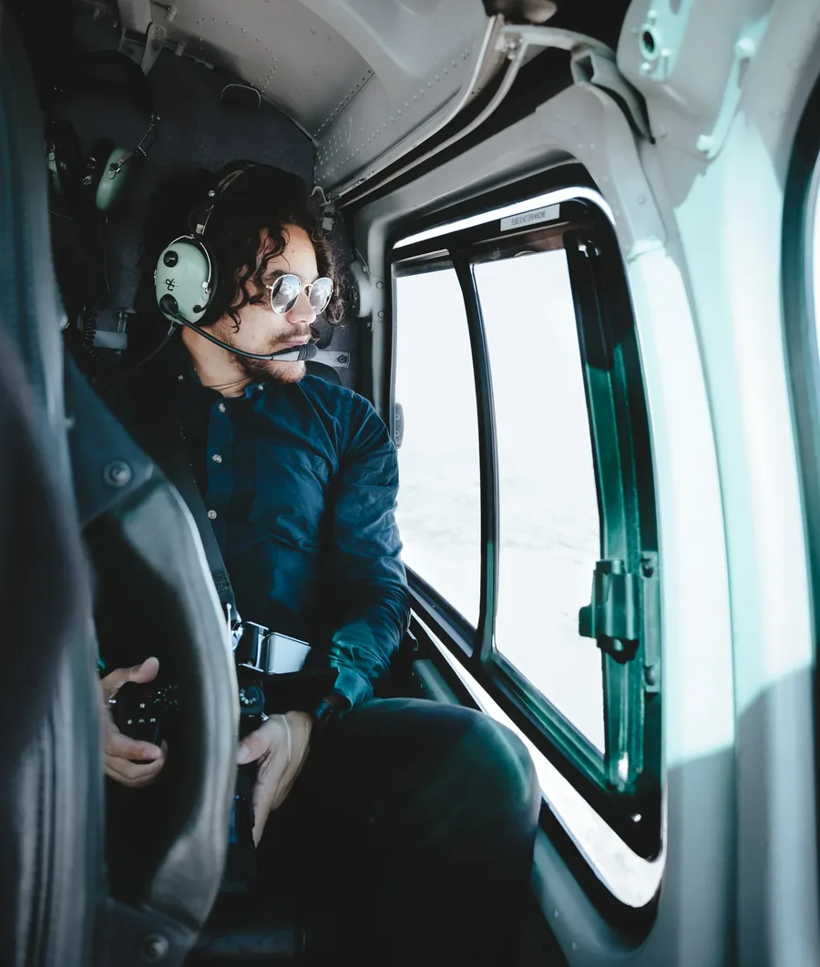 Cristian Batista wearing sunglasses and a headset, seated in the cockpit of a helicopter.