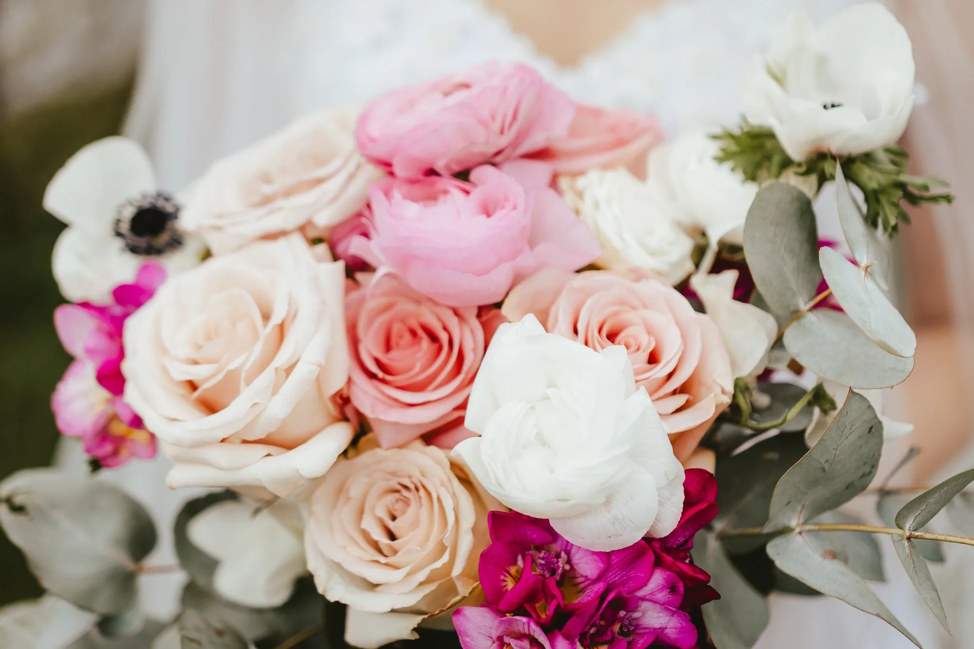 A soft bridal bouquet of pink and white roses, anemones and eucalyptus held by a bride