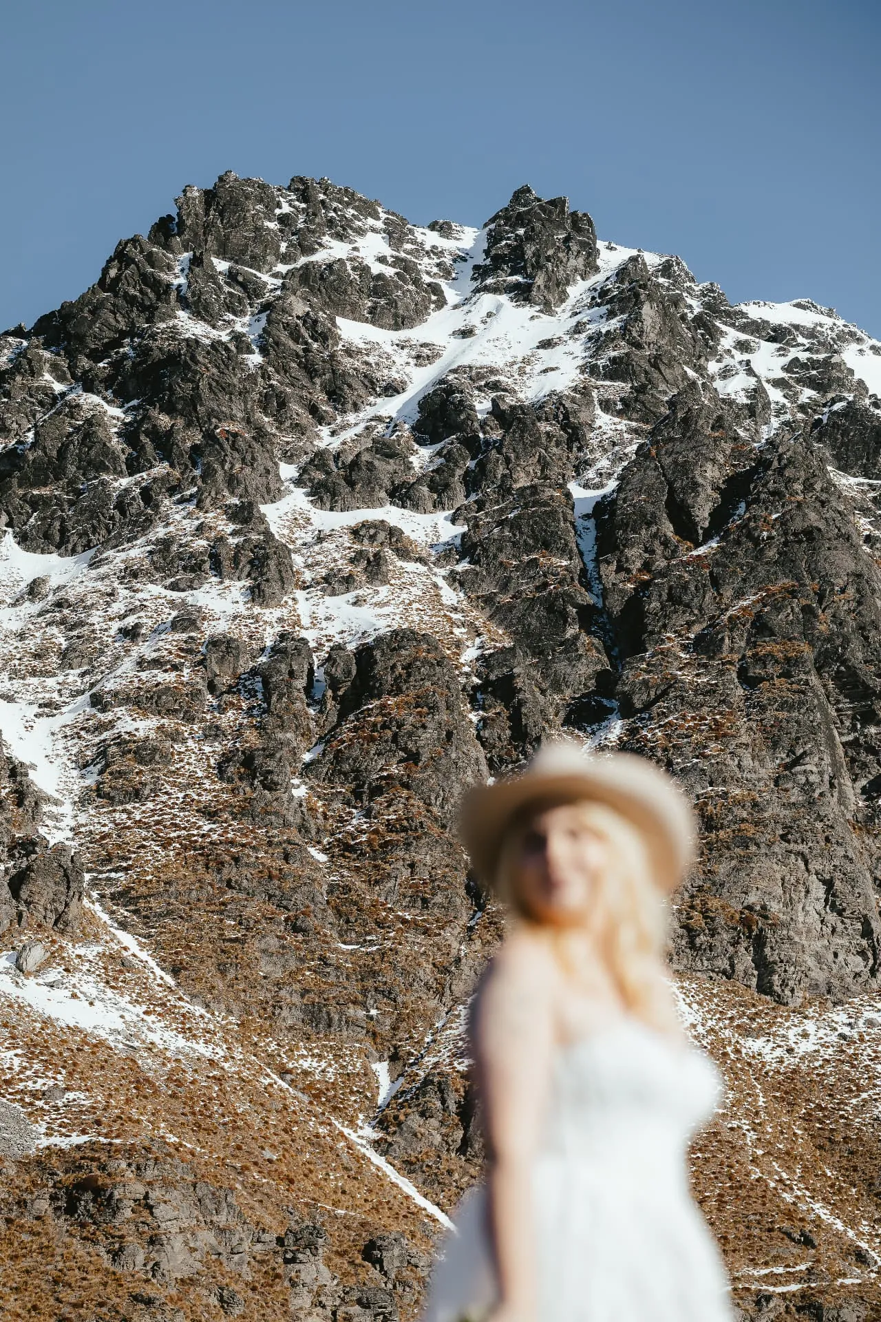 Bride in a hat with the snow-dusted summit of Cecil Peak behind her, spring heli elopement.