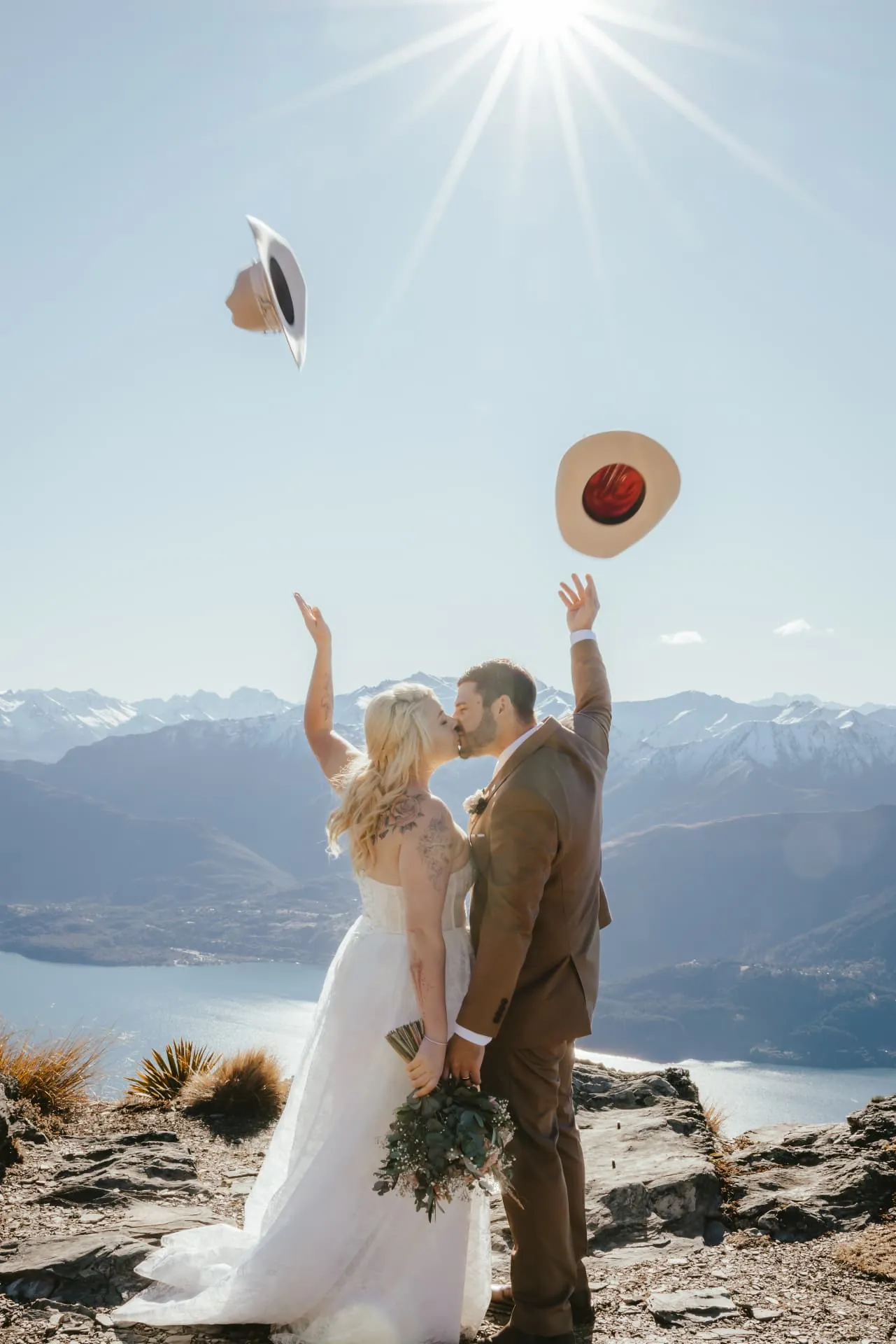 Couple throwing their hats into the air in celebration on Cecil Peak under a bright spring sun.
