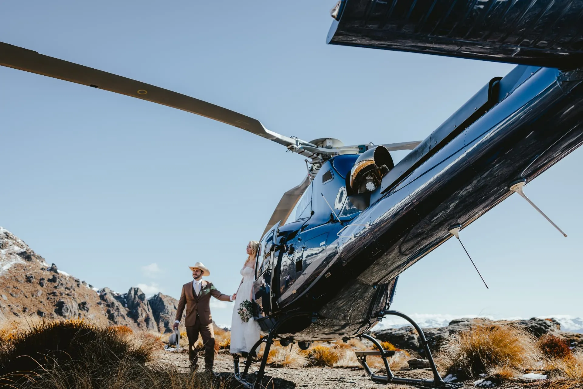 Couple walking from the helicopter after landing on Cecil Peak for their spring wedding, Queenstown.
