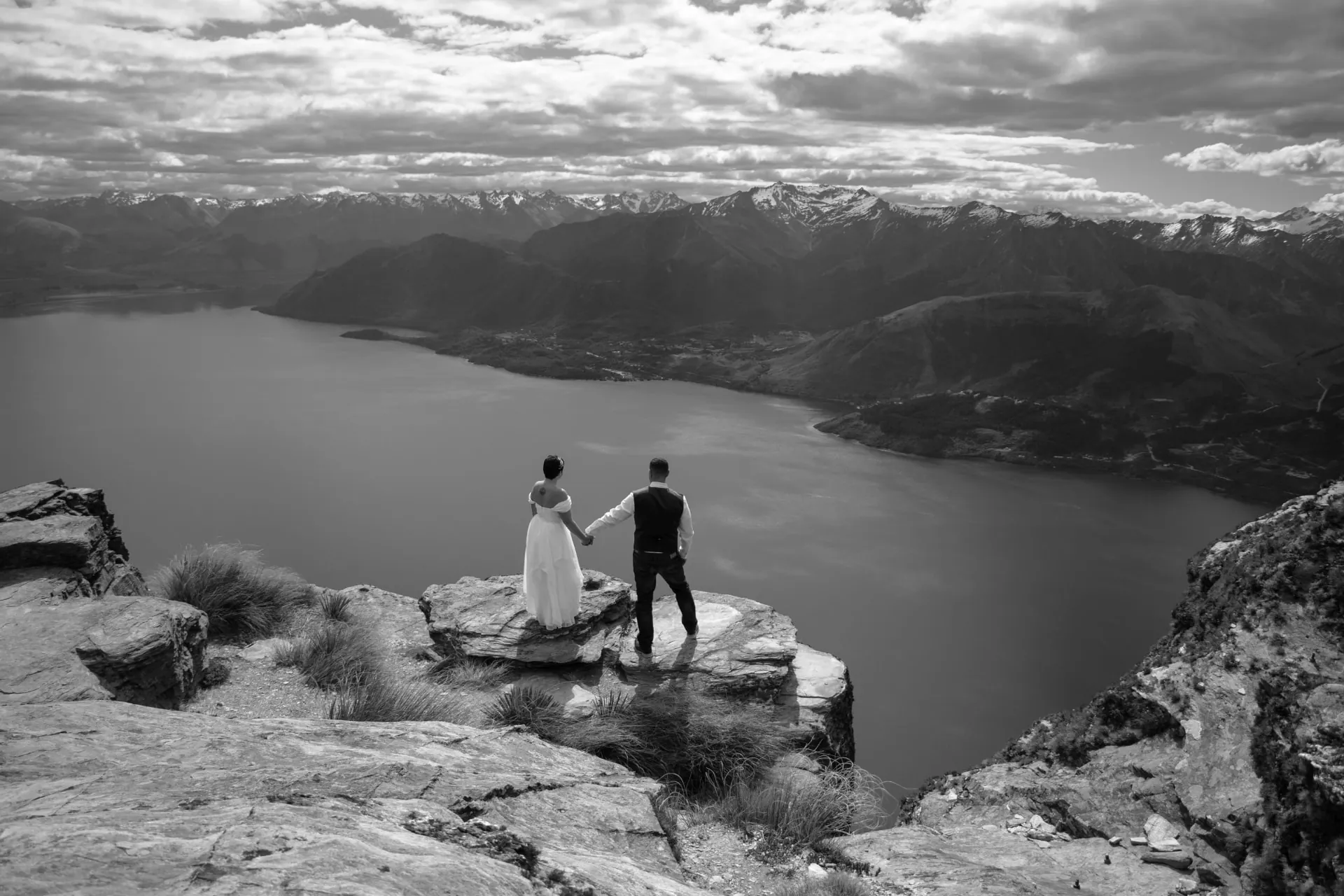 Black and white photo of a couple on the cliff edge at Cecil Peak Ledge above Lake Wakatipu.