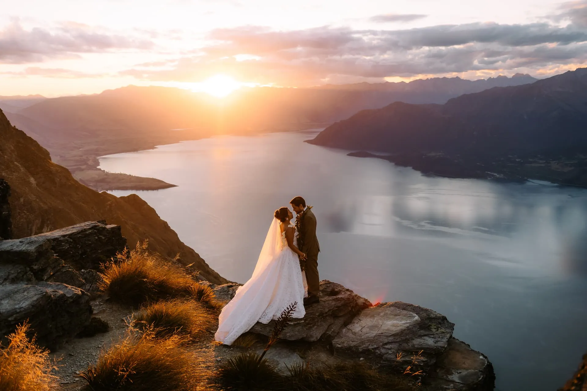 Couple embracing on the Cecil Peak Ledge in golden hour light, Lake Wakatipu and the Southern Alps beyond.