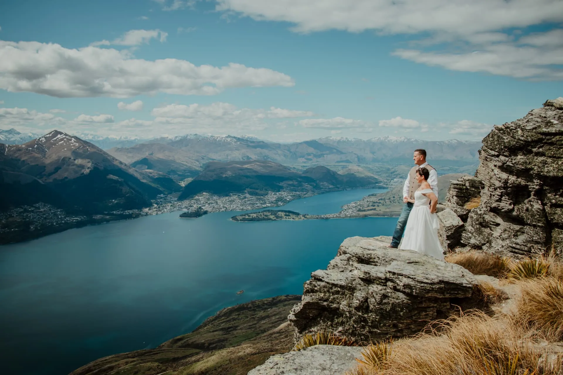 Couple embracing on the Cecil Peak Ledge by day, Lake Wakatipu and Queenstown below.