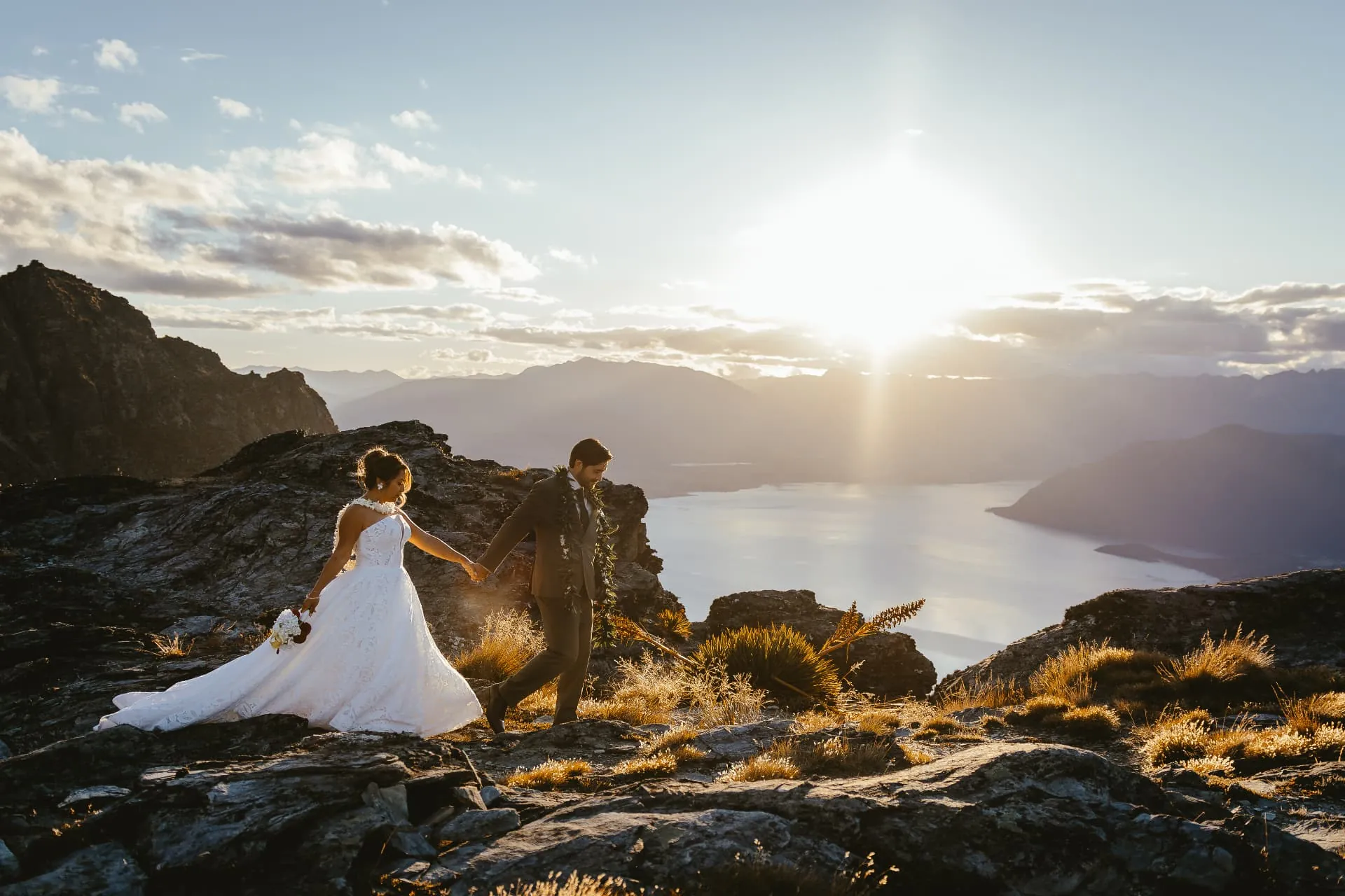 Heli elopement couple on the rocky Ledge at Cecil Peak, Queenstown, with the sun setting over Lake Wakatipu.