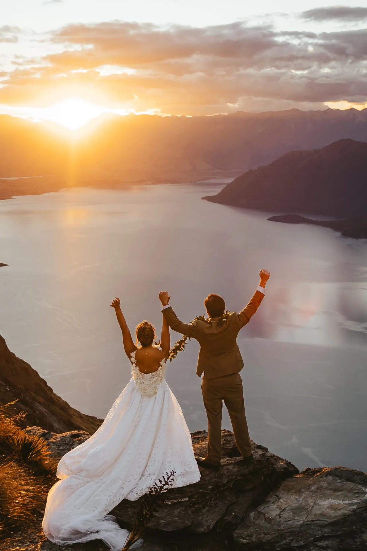 Just married couple raising their arms in celebration on the Cecil Peak Ledge at sunset.