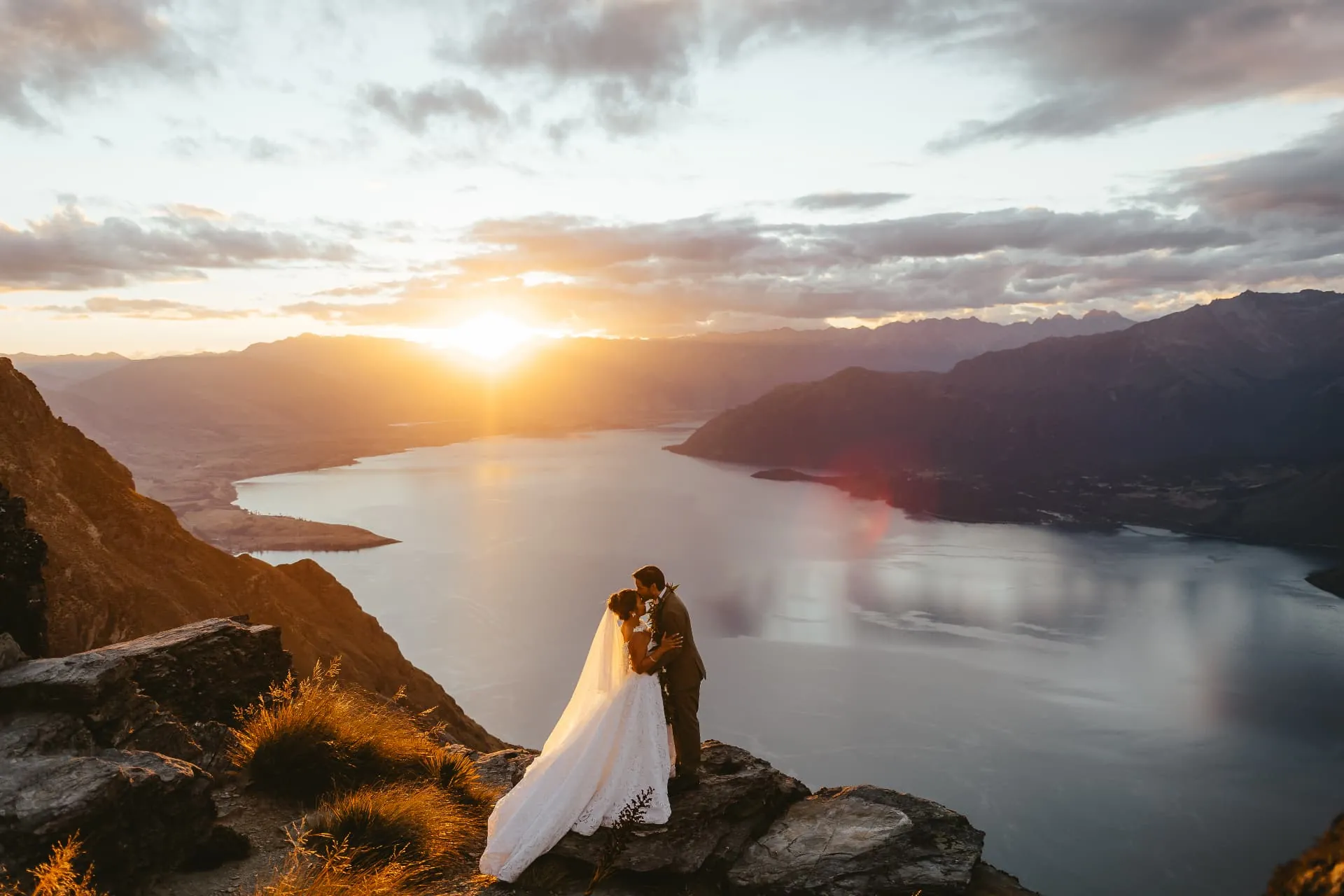 Queenstown heli elopement on the Cecil Peak Ledge at sunset, the couple small against the lake and mountains.