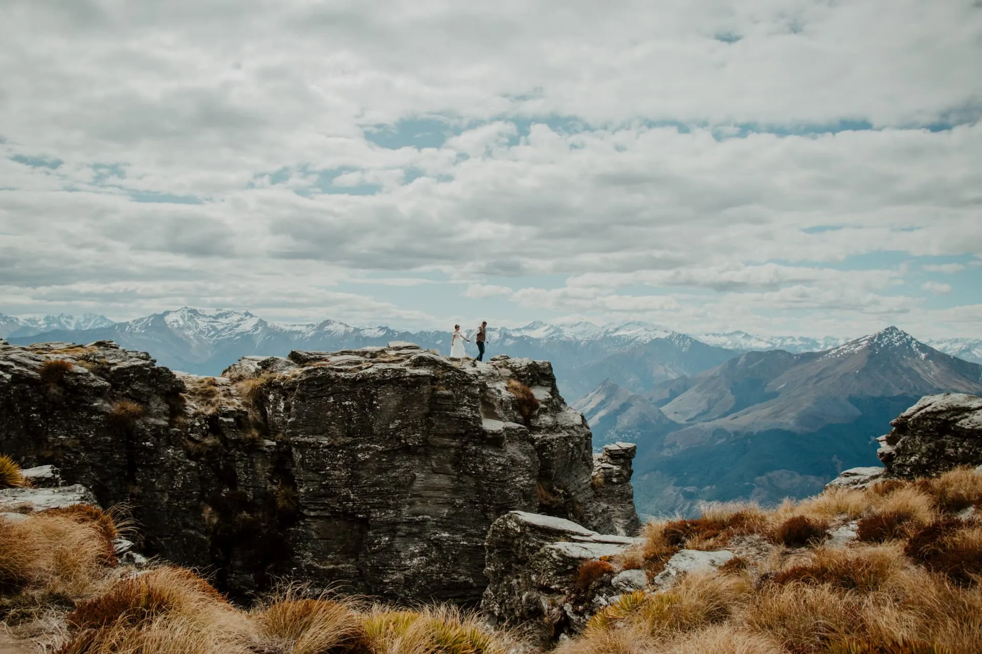 Wide landscape of a couple on top of the rocks at Cecil Peak Ledge, mountains and big sky beyond.