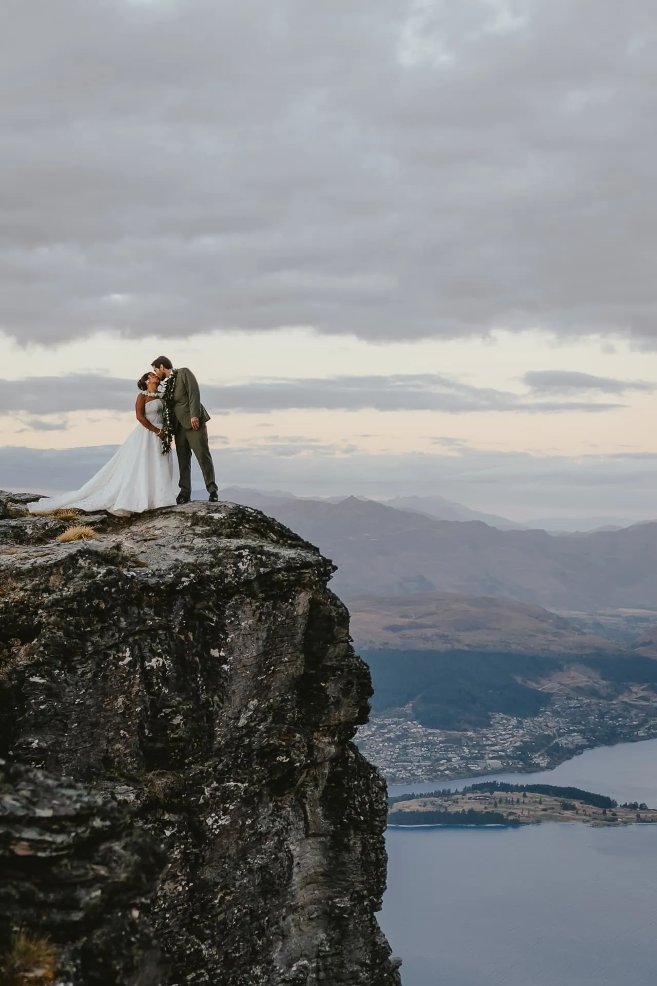 Couple kissing on a rock pinnacle at Cecil Peak with Queenstown and Lake Wakatipu far below.