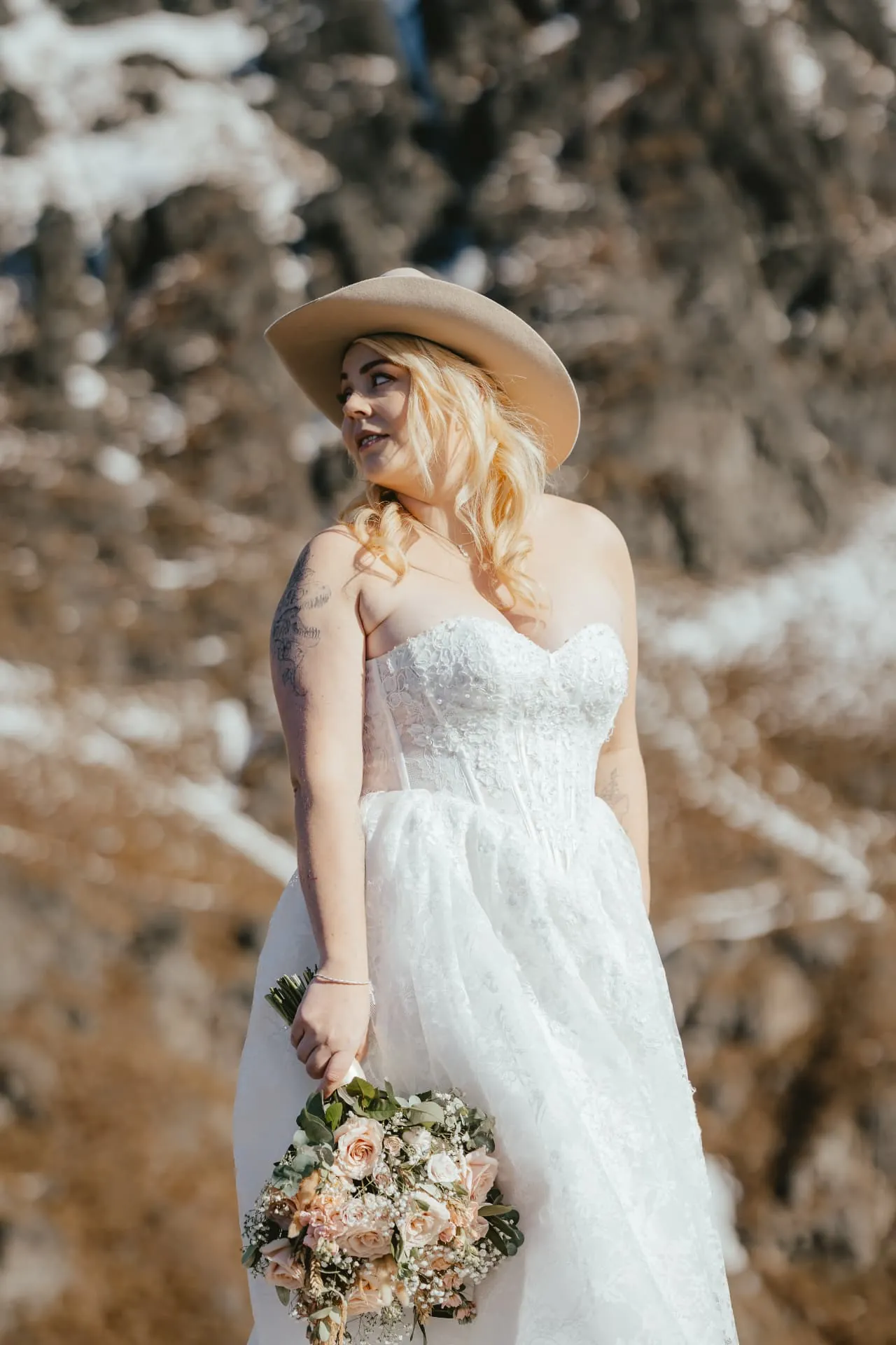 Spring bride holding her bouquet in front of snowy rock on Cecil Peak, Queenstown.