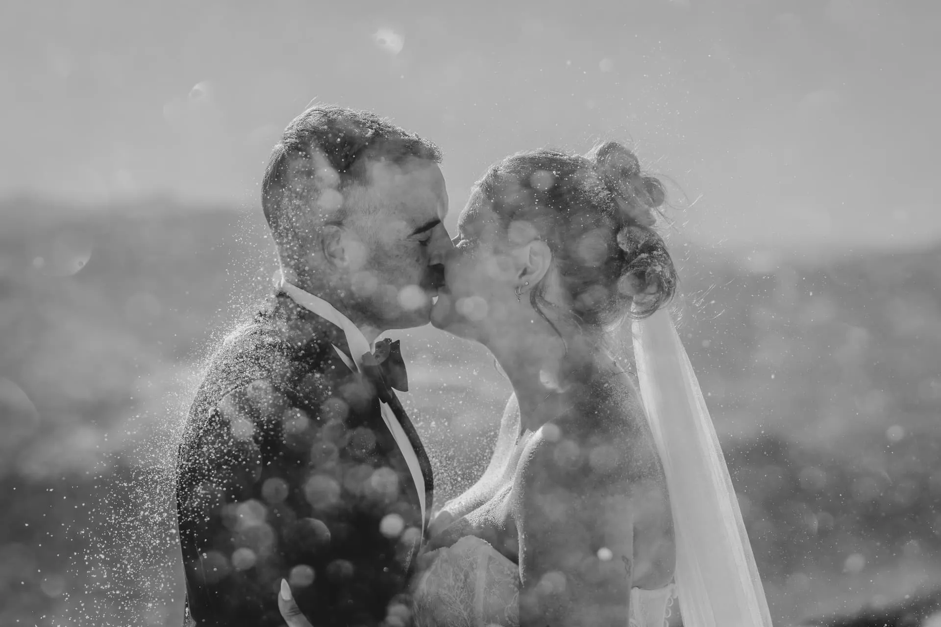 Black and white photo of a couple kissing through falling snow on Cecil Peak.