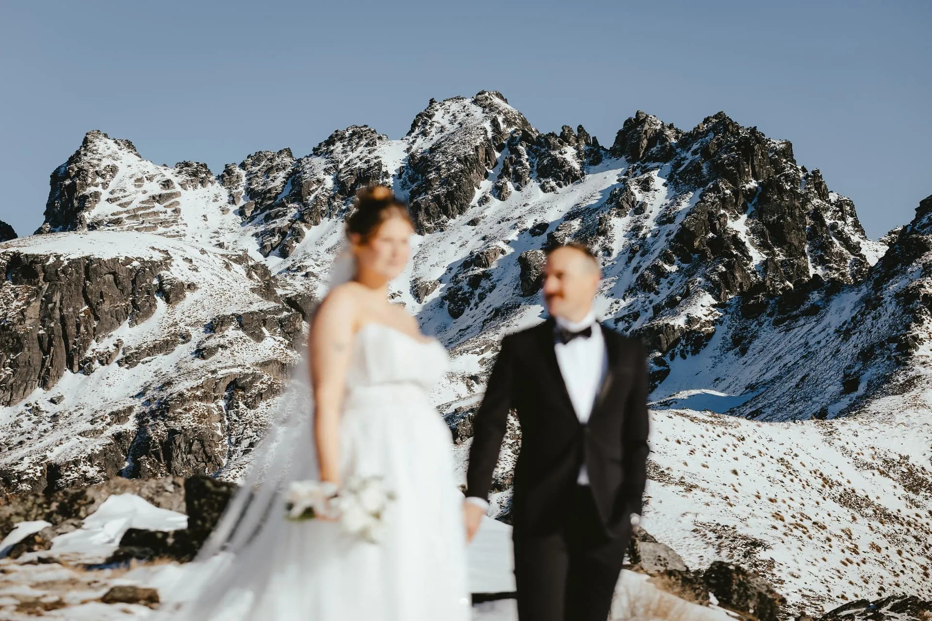 Couple standing together in the snow on Cecil Peak beneath jagged snow-covered rock peaks.
