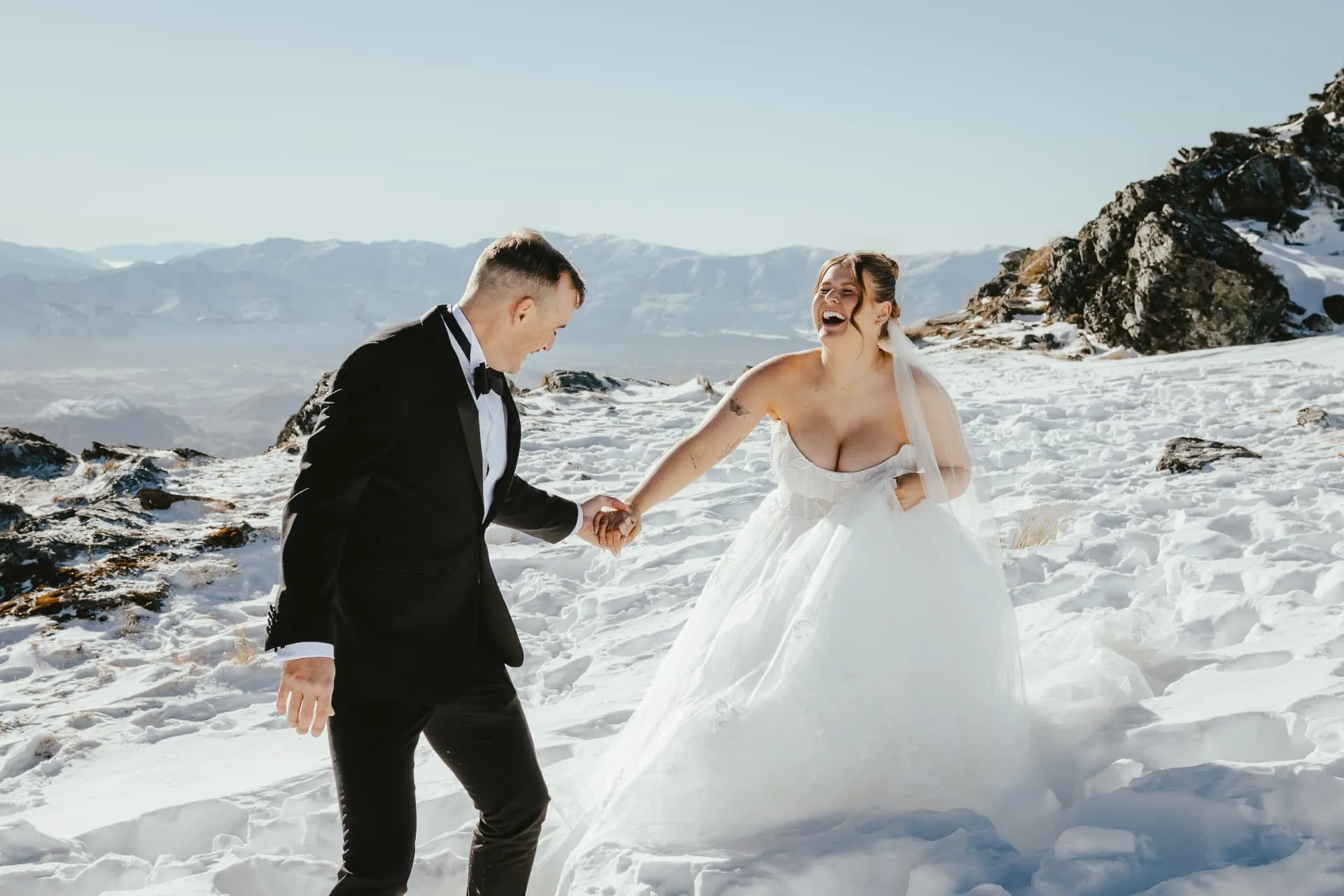 Groom leading his bride through deep snow on the Spur at Cecil Peak, Queenstown, in late winter.