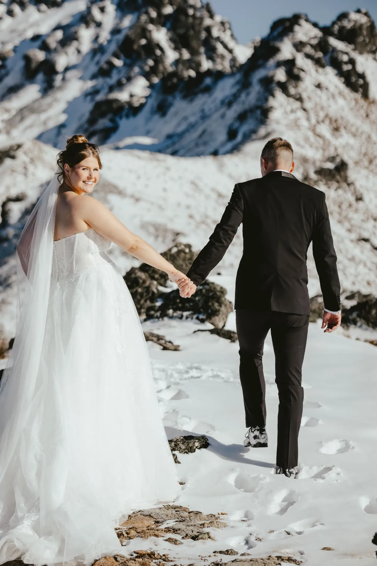 Couple walking hand in hand across the snowfield on the Spur at Cecil Peak, rocky peaks behind.