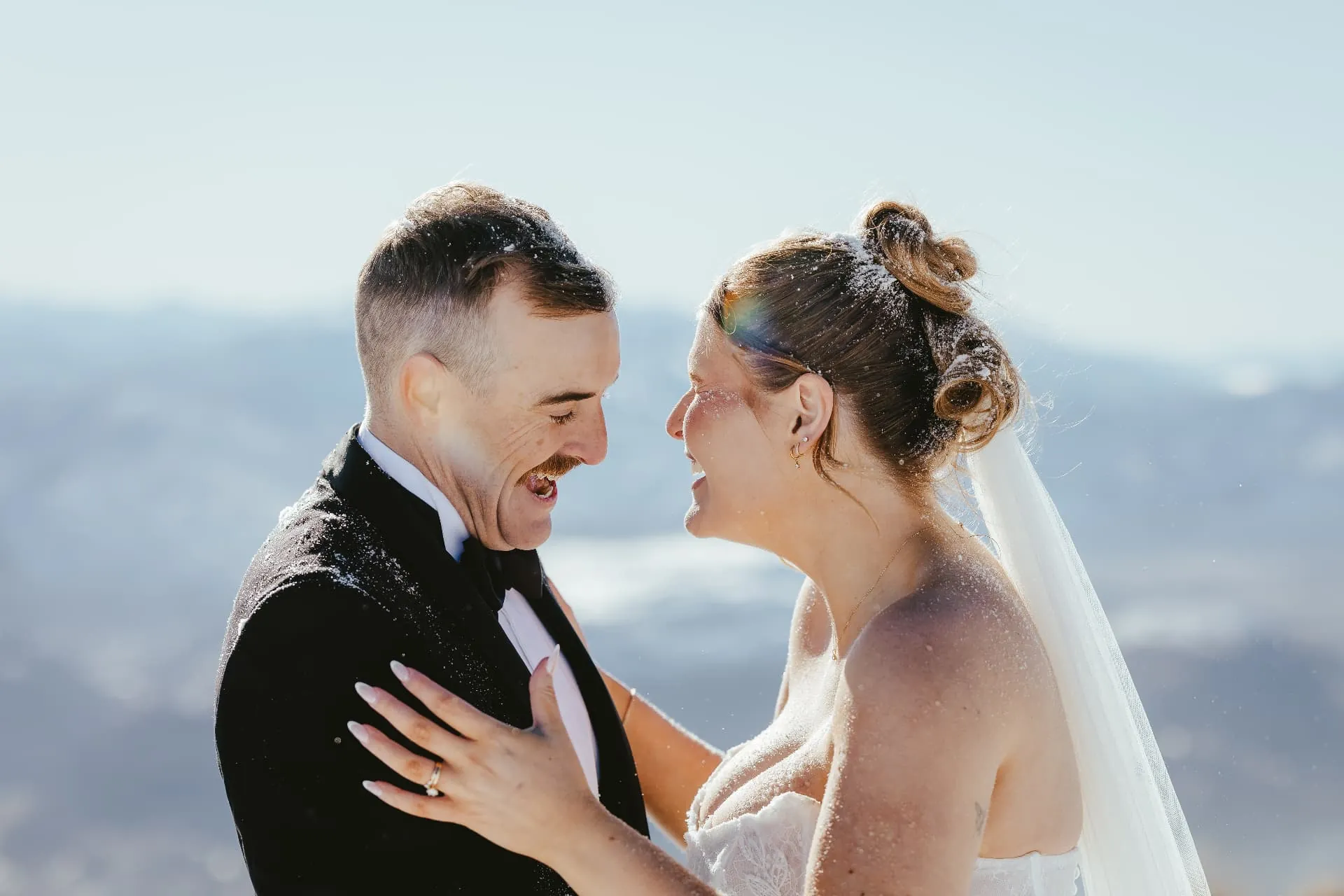 Bride and groom laughing together, snow in their hair, on a winter Cecil Peak elopement.