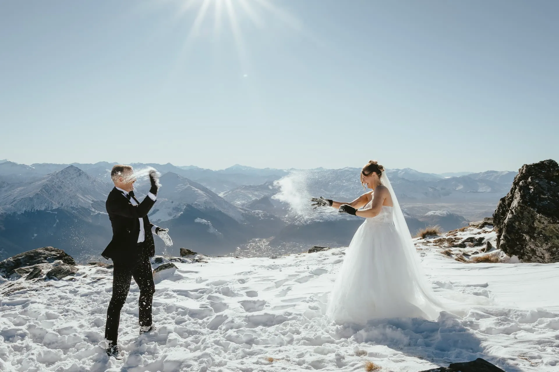 Bride and groom having a snowball fight on the snowy Spur at Cecil Peak, mountains behind.