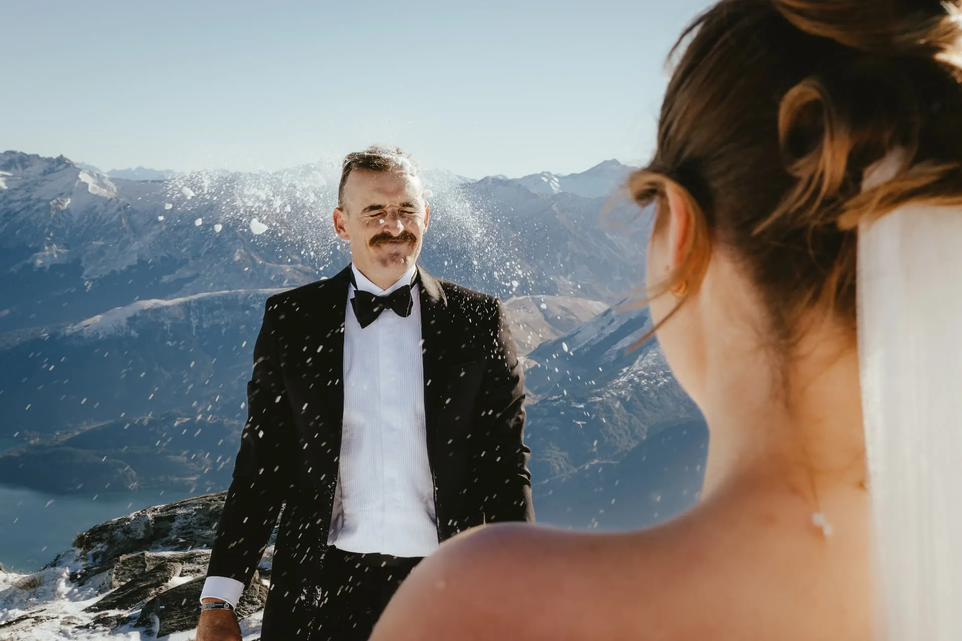Groom laughing as a snowball bursts on his tux on the Cecil Peak Spur.