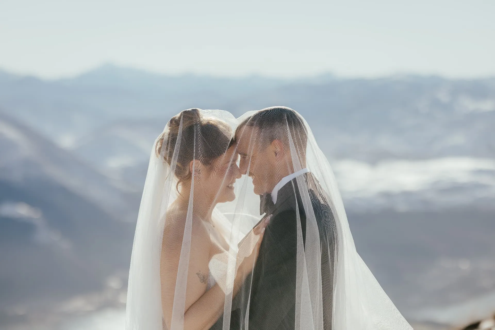 Close portrait of a couple under the bride\u2019s veil on Cecil Peak, soft winter light and mountains beyond.