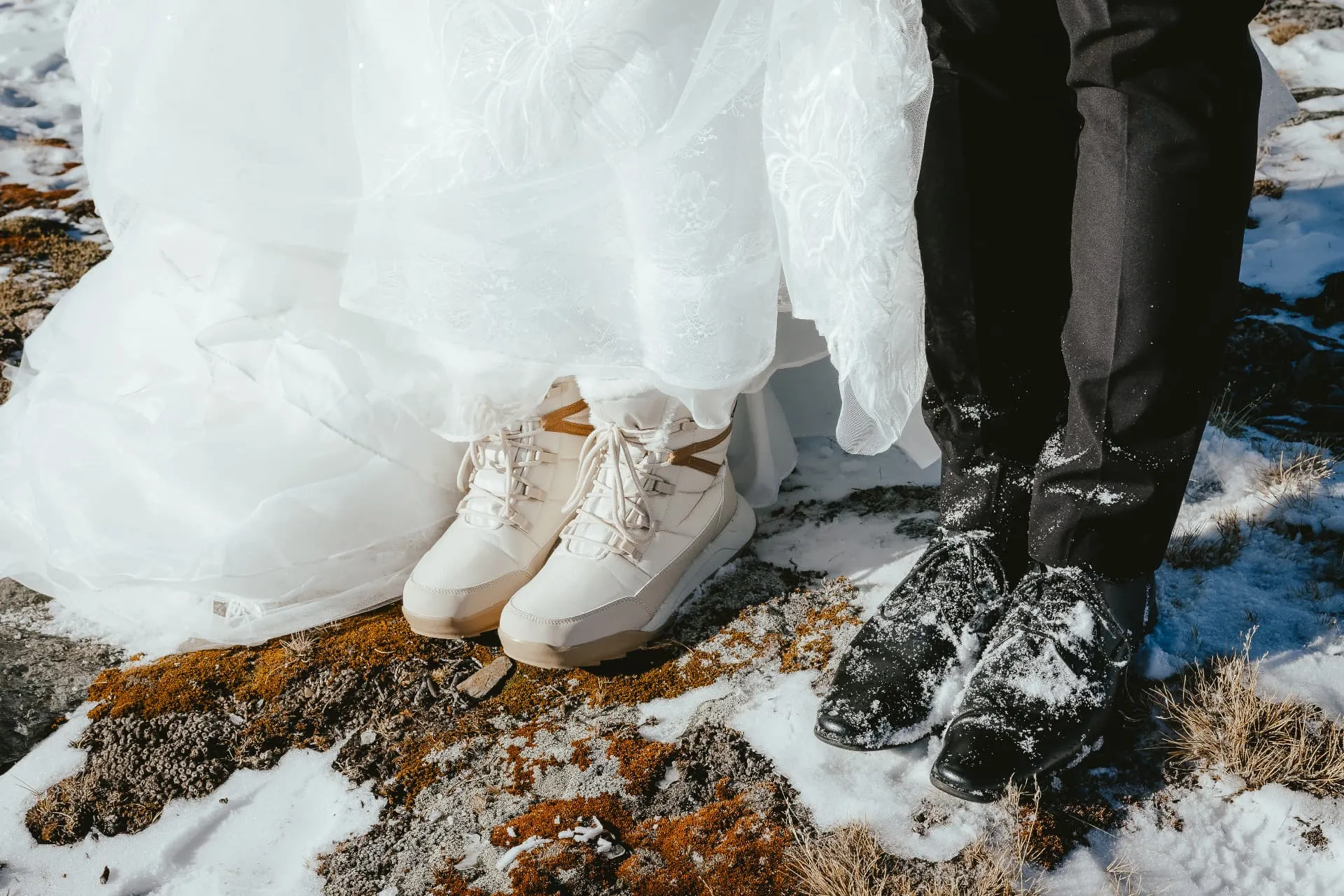 Detail of the bride\u2019s white sneakers and the groom\u2019s shoes in the snow on Cecil Peak.
