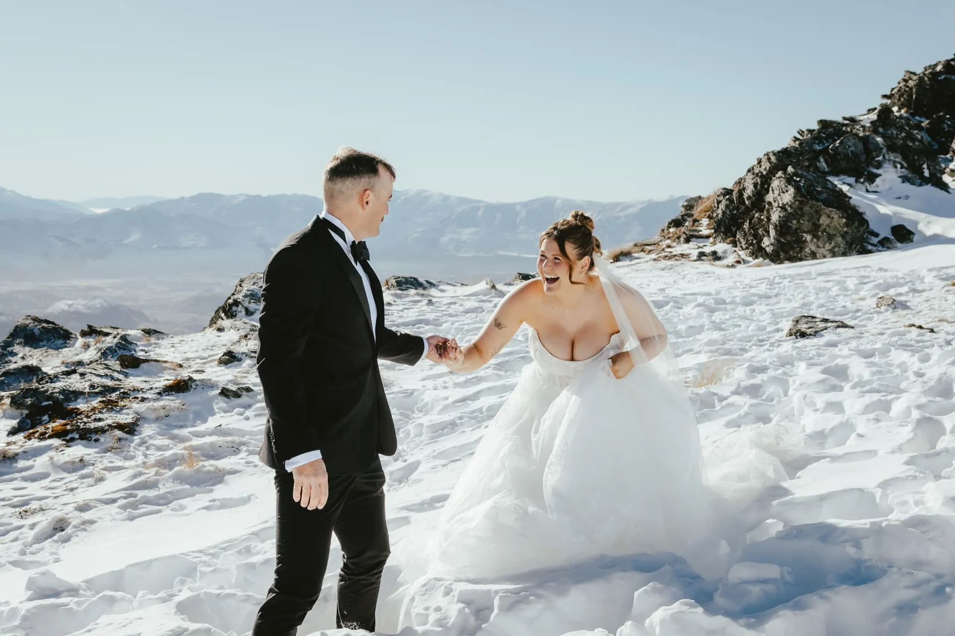Couple laughing and holding hands in fresh snow on the Cecil Peak Spur, end of winter.