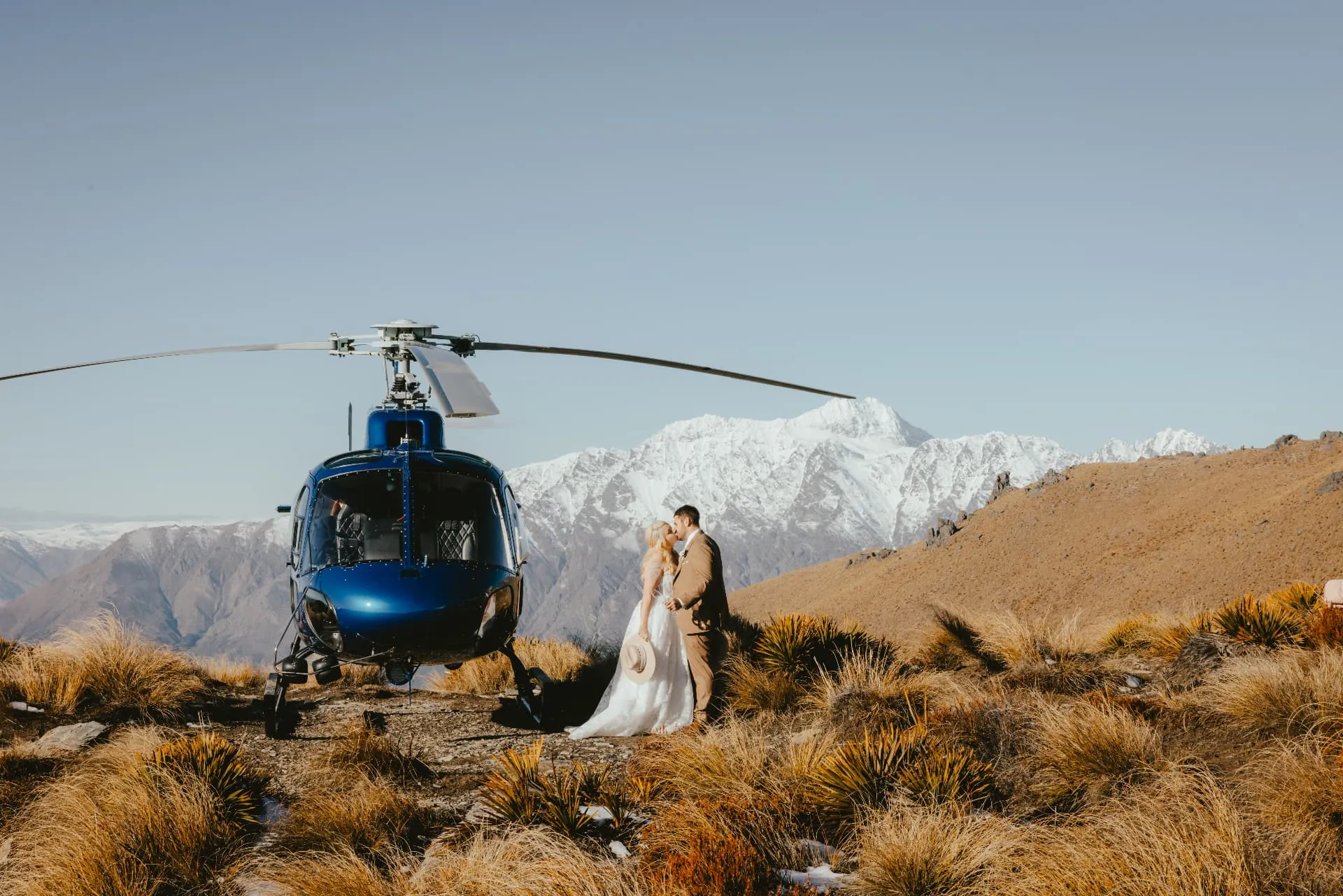 Wide spring view of a couple on the summit rock of Cecil Peak above Lake Wakatipu.