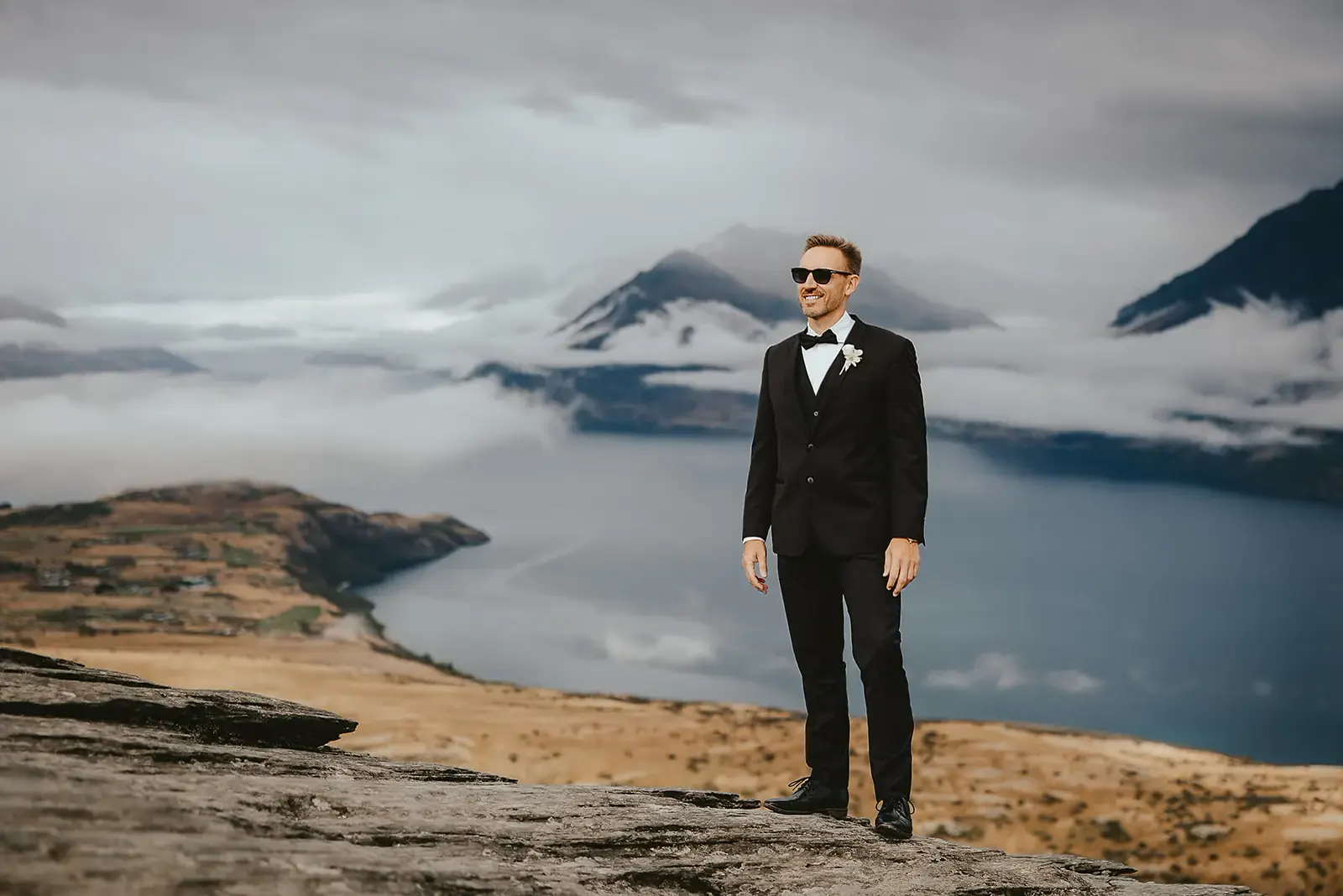 Groom on a schist ledge at Deer Park Heights with the lake and cloud behind