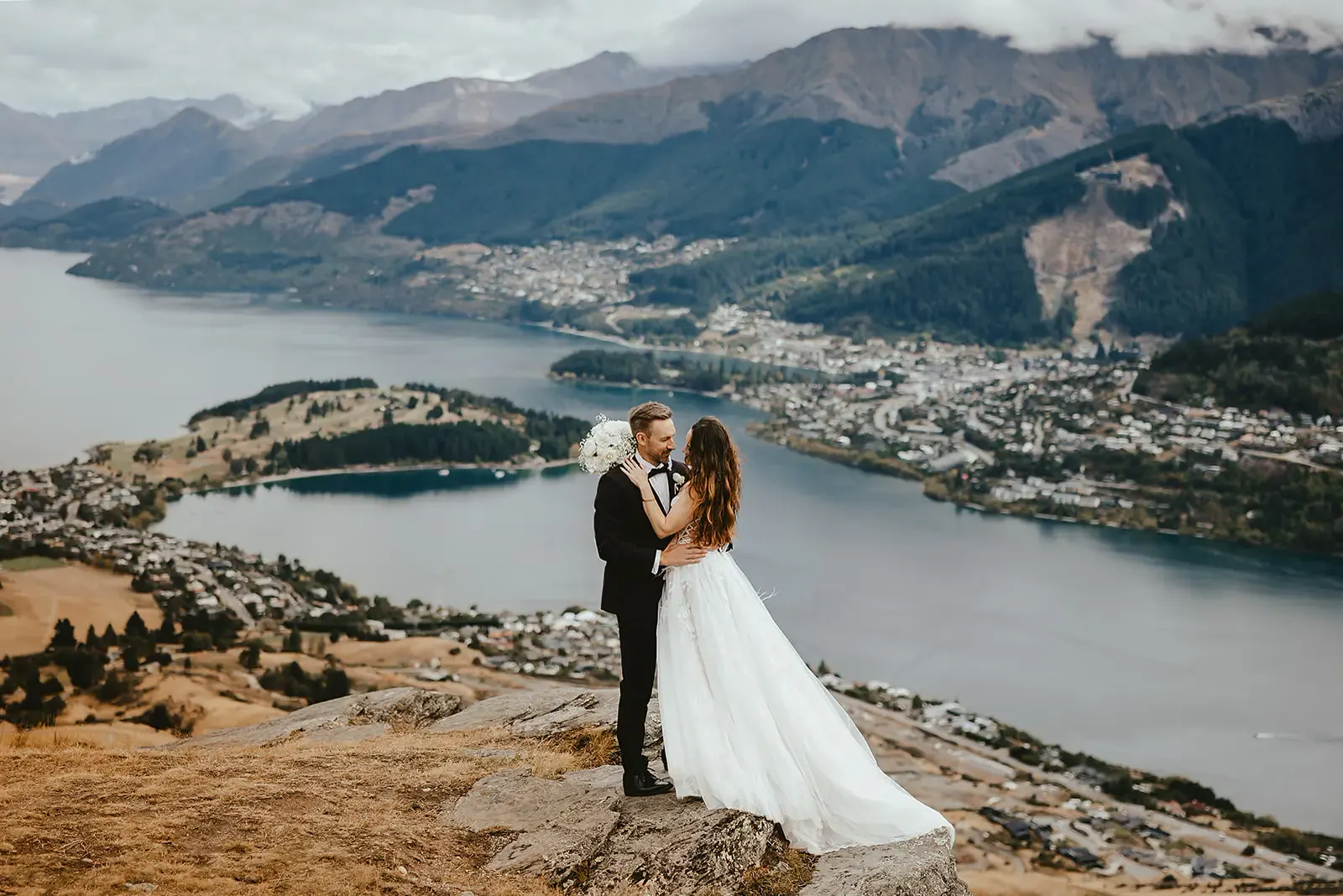 Bride and groom on a schist outcrop at Deer Park Heights, Queenstown, with the Frankton Arm and Lake Whakatipu below