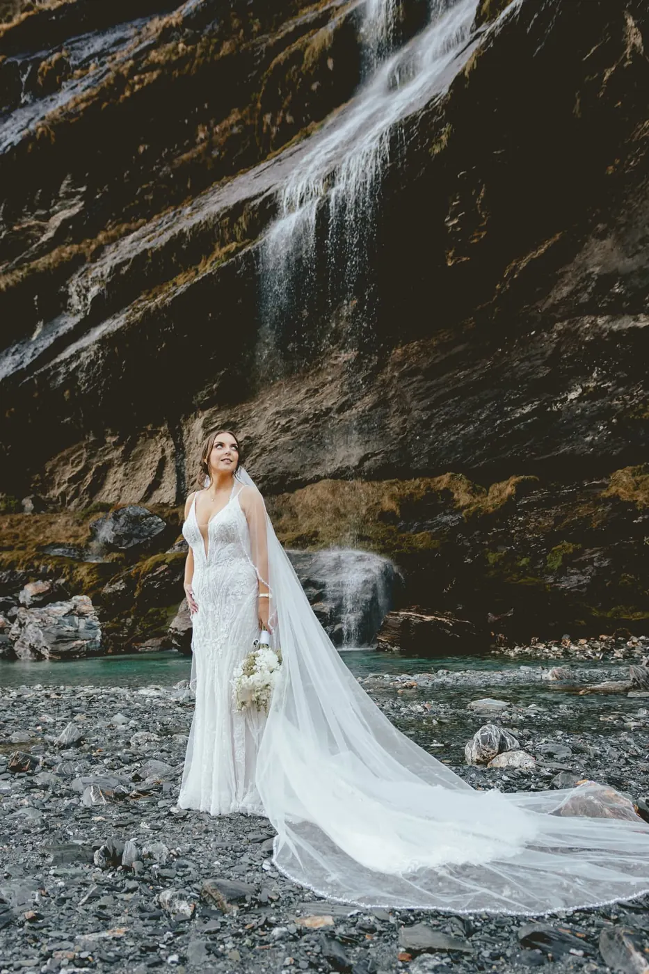 Bride looking up at the main Earnslaw Burn waterfall as it falls into a turquoise pool at the start of winter