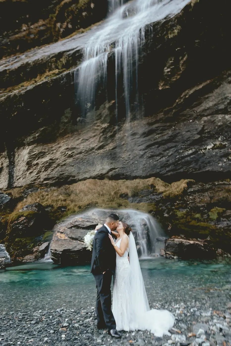 Bride and groom kissing at the turquoise pool below the main Earnslaw Burn waterfall in early winter