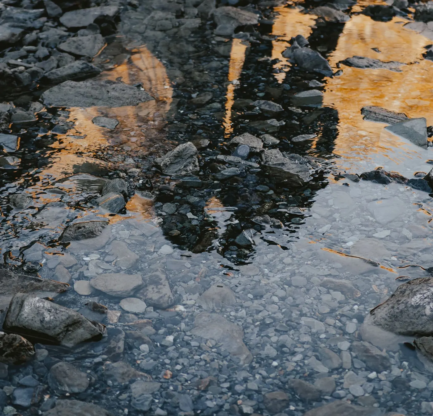Reflection of a bride and groom in a still glacier-fed pool at Earnslaw Burn, lit gold by low winter sun