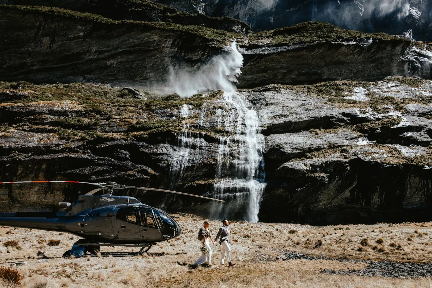 Couple walking from the helicopter across the Earnslaw Burn basin towards the waterfalls.