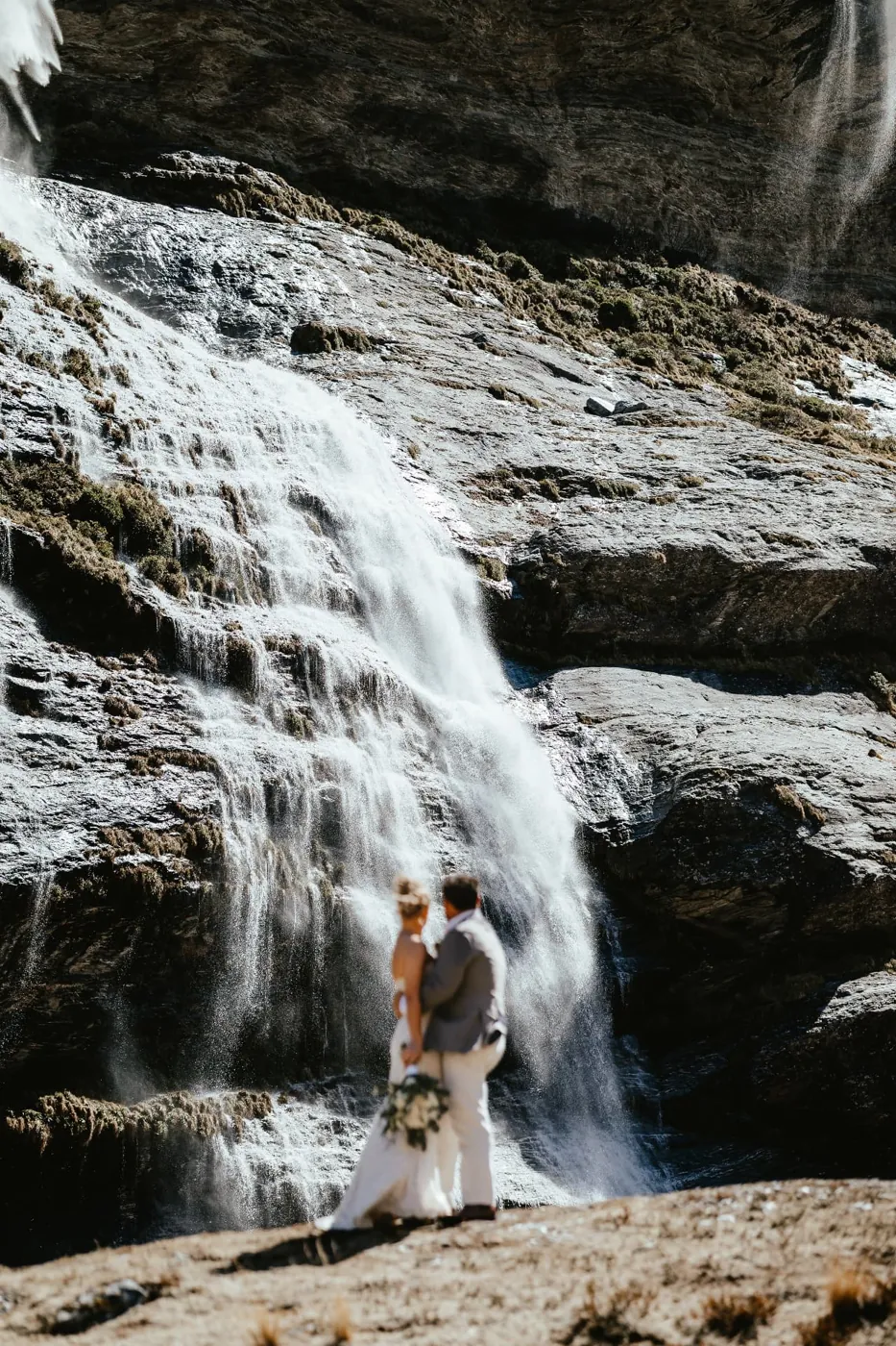 Bride and groom embracing in front of an Earnslaw Burn waterfall, New Zealand.