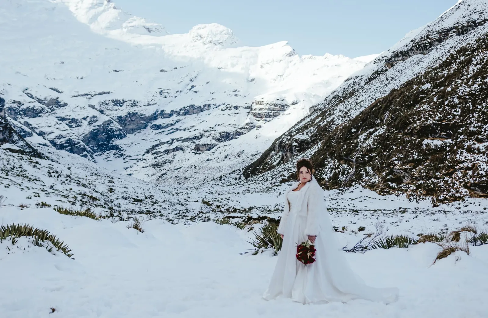 Bride in a white fur wrap holding red roses in the snowy Earnslaw Burn valley in winter