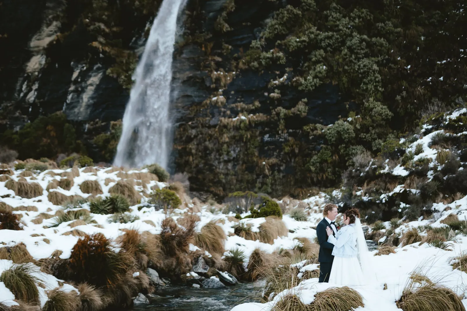 Couple embracing in the snow below the lower Earnslaw Burn waterfall, which keeps flowing in winter