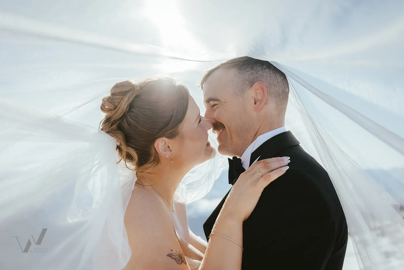 Newlyweds kissing under a veil in the sunlight