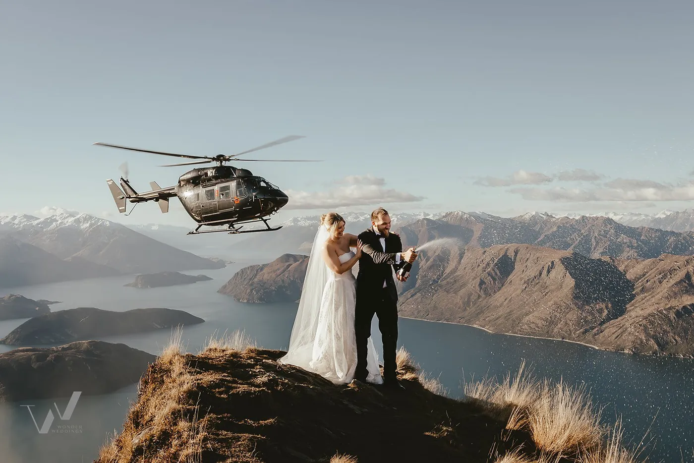 Bride and groom beside a helicopter on a tussock ridge, Queenstown