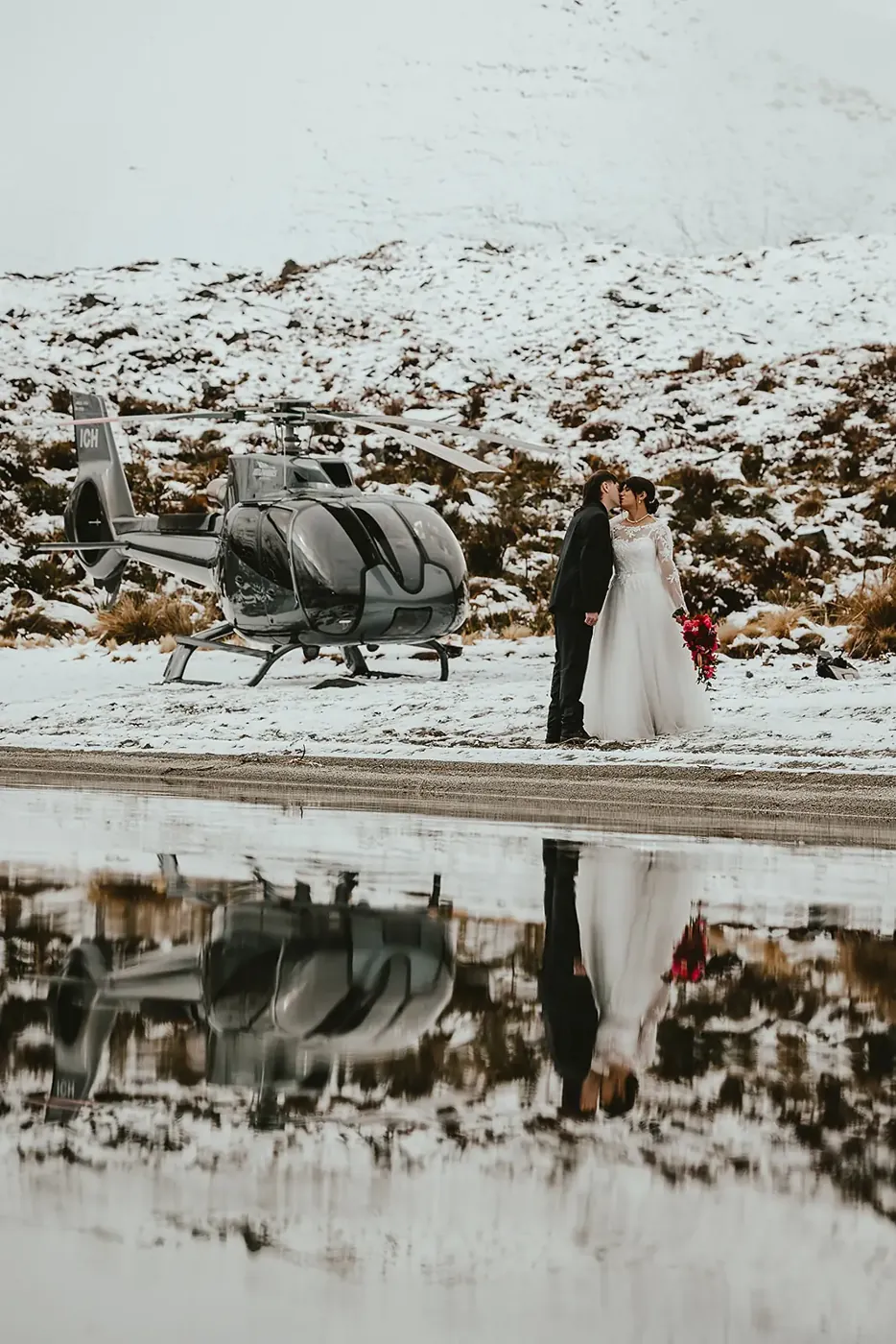 Bride and groom beside a helicopter at Lake Lochnagar, reflected in the lake in spring