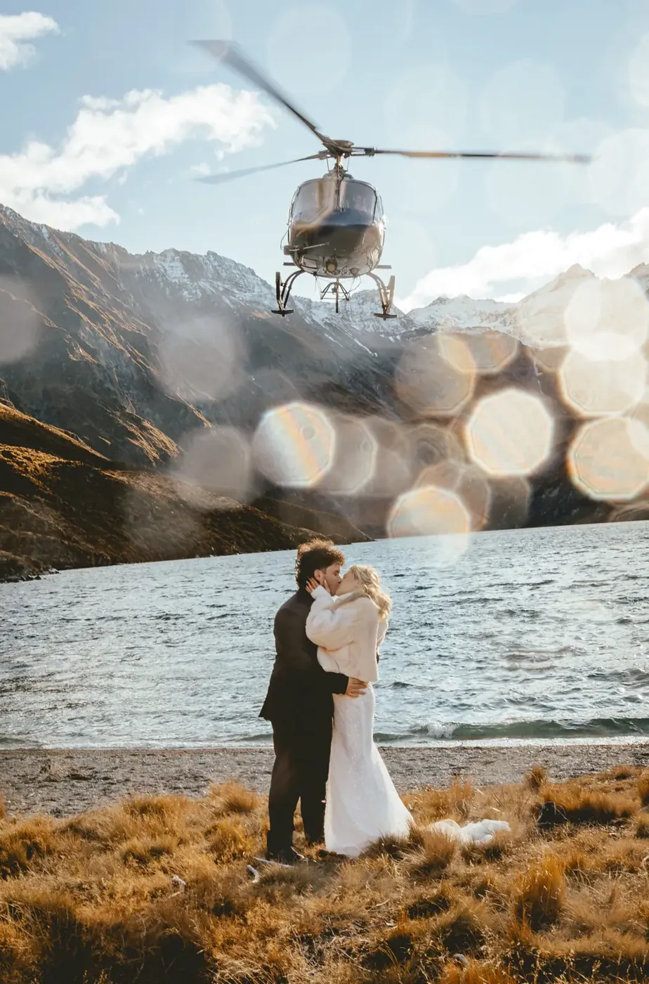 Couple kissing in golden tussock at Lake Lochnagar as a helicopter hovers above