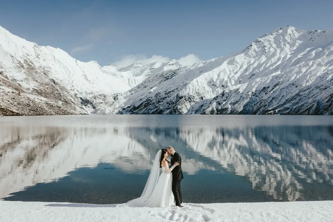 Couple kissing on snow at Lake Lochnagar with snowy mountains reflected in the water