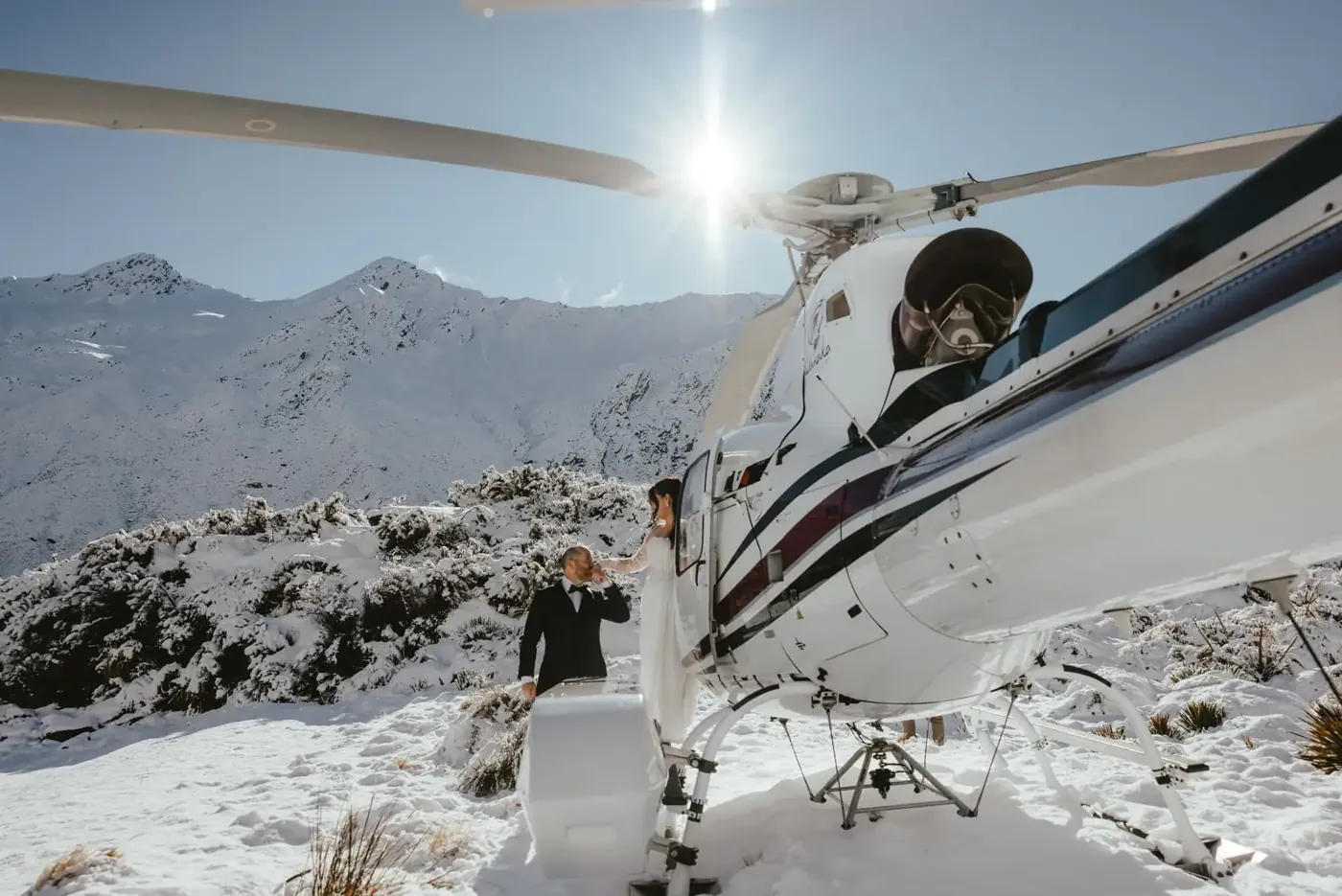 Groom kissing the bride's hand beside a helicopter in the snow at Lake Lochnagar