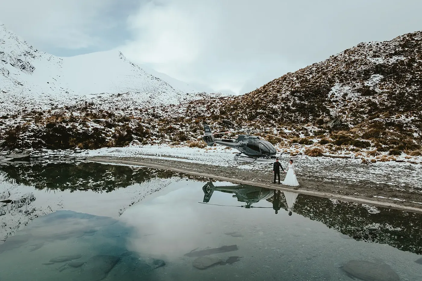 Helicopter landed on the snowy shore of Lake Lochnagar in spring, mirrored in the still lake