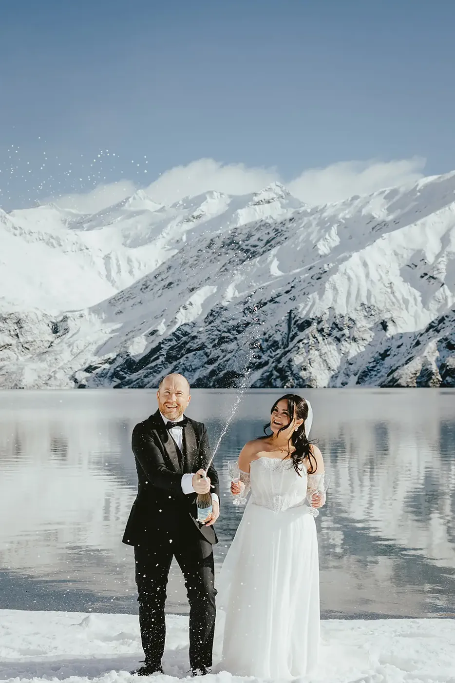 Couple spraying champagne at Lake Lochnagar with snowy peaks behind