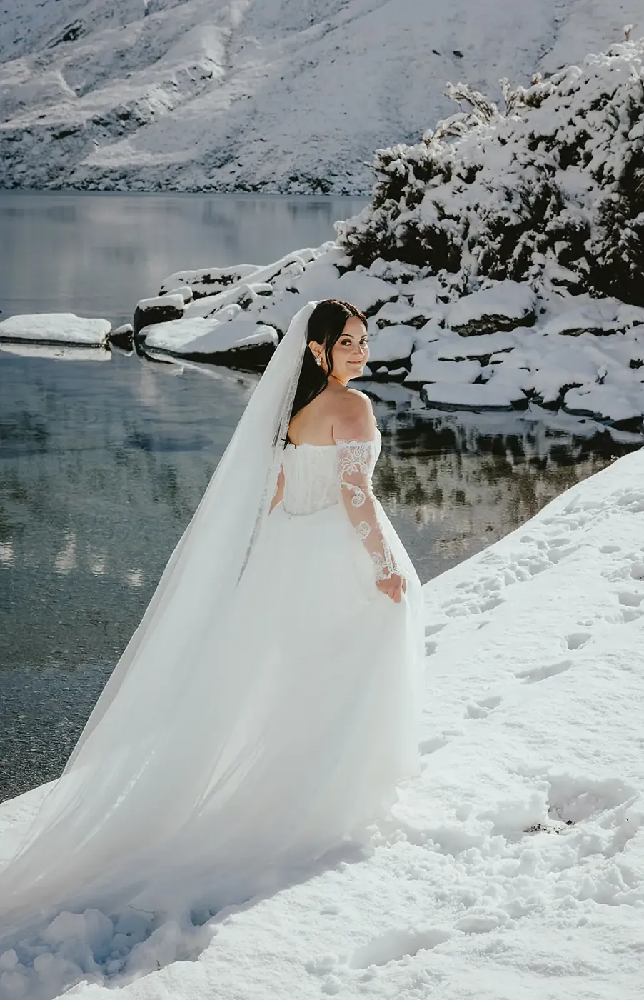 Bride with a long veil on the snowy shore of Lake Lochnagar