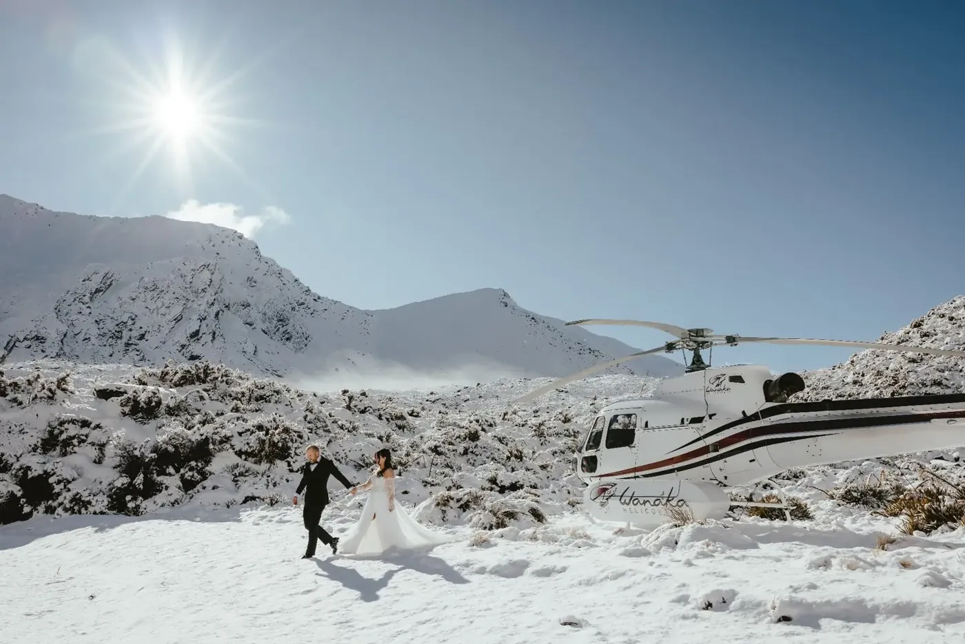 Bride and groom walking through fresh snow towards a helicopter at Lake Lochnagar in winter