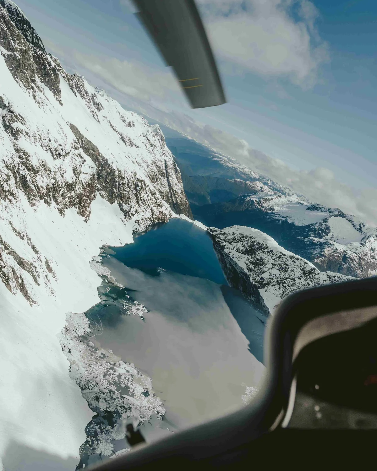 Snow-covered mountains and an alpine lake seen from a helicopter window.