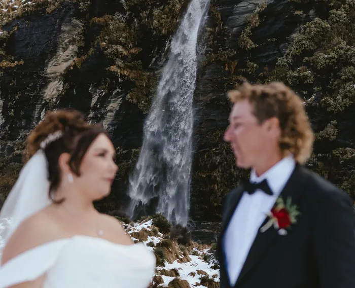 A bride and groom smiling at each other in front of an alpine waterfall.