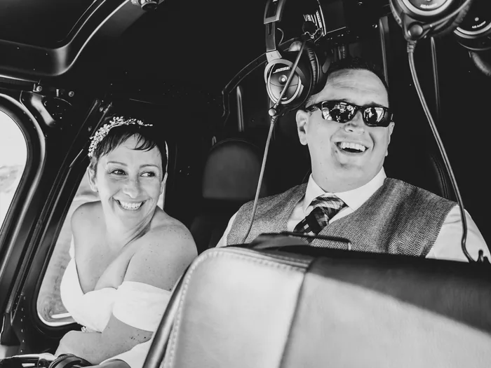 Black and white photo of a bride and groom laughing inside a helicopter.