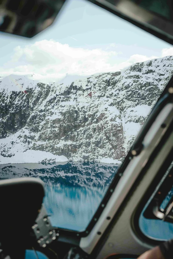 Snow-covered peaks and an alpine lake seen from a helicopter cockpit.
