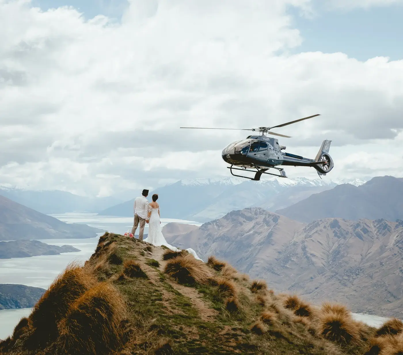 Couple on an alpine summit as the helicopter arrives for the next landing.