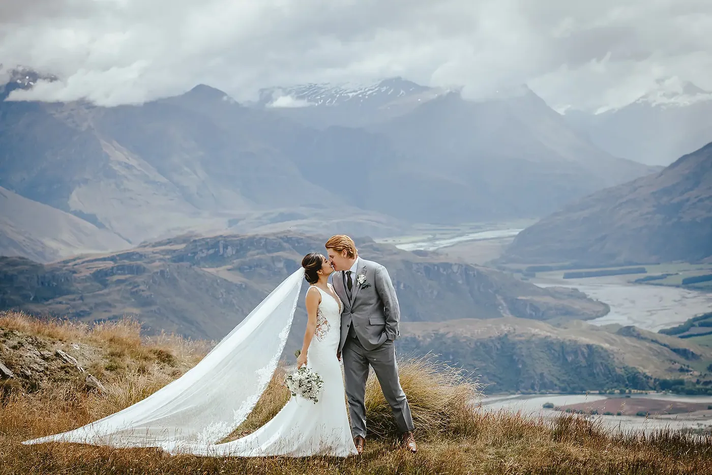 A couple kissing on Coromandel Peak with a veil flowing over the Wānaka valley.